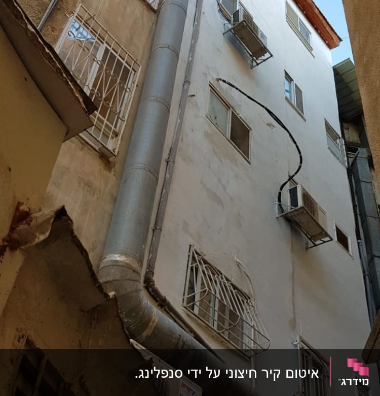 צינור מתכת גדול על קיר בניין עם מזגנים